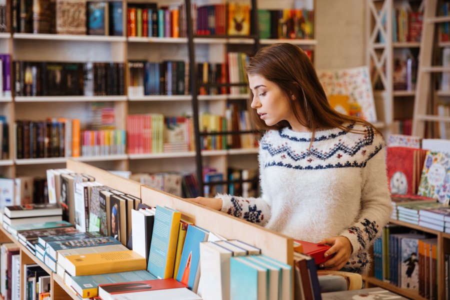 Ragazza sfoglia i libri in una libreria tra le novità editoriali e i libri in uscita a giugno